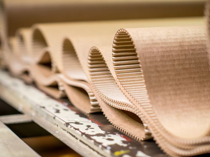 Nahaufnahme von aufgerollten Wellpappbögen auf einem Tisch, die die Schichten und Wellen des Materials hervorheben.